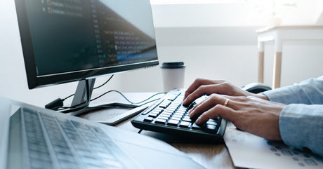 A person sitting at a desk typing on a keyboard. The computer screen is in the background.