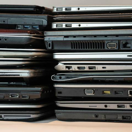 A stack of laptops piled together with various ports, vents, and designs visible from different models and brands.