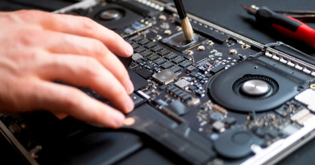 A close-up of the inside of a laptop with several tools nearby. Someone is using a brush to clean the processor.