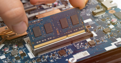 A person inserting a RAM module into a blue motherboard inside a computer with visible components and circuits.