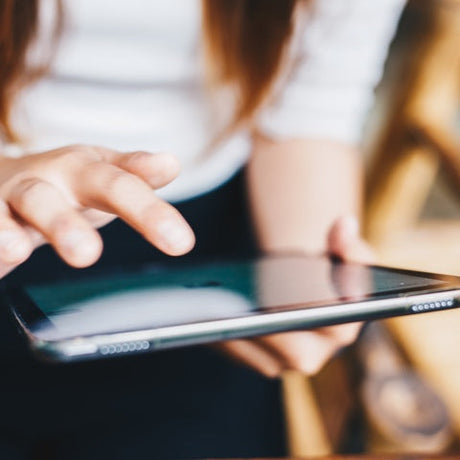 A woman with brown hair wearing a white rolled up long-sleeve shirt and bracelet using an Apple iPad device.