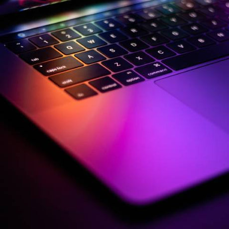 A MacBook keyboard and trackpad with visible command keys under a vibrant pink, orange, and purple glow.
