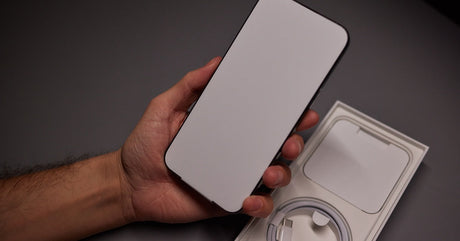 A person holding new smartphone above open box with USB-C charging cable and accessories on dark surface.