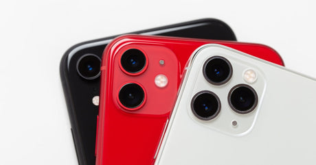 A close-up view shows the back camera on a white, a red, and a black Apple iPhone. The background is white.