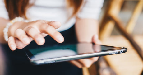 A close-up view shows a woman holding a black iPad in one hand while using a finger to press the screen.