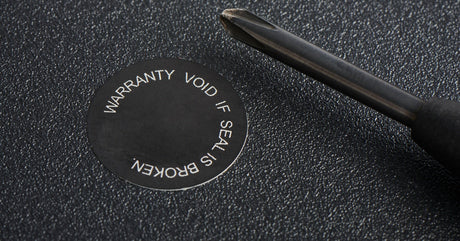 A close-up view shows a black screwdriver sitting on a black surface. A small sticker reads "warranty void if seal broken."