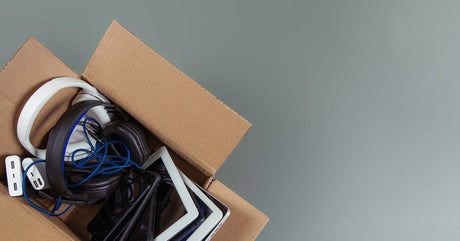 A cardboard box is full of cables, charging bricks, cellphones, tablets, and headphones. The box is open.