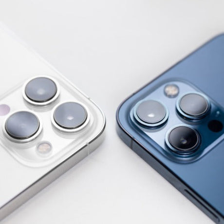 A close-up view shows a white iPhone and a dark teal iPhone lying screen side down on a white background.